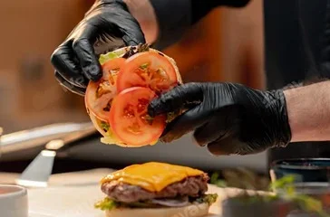 Gloved chef slicing a fresh tomato for food preparation